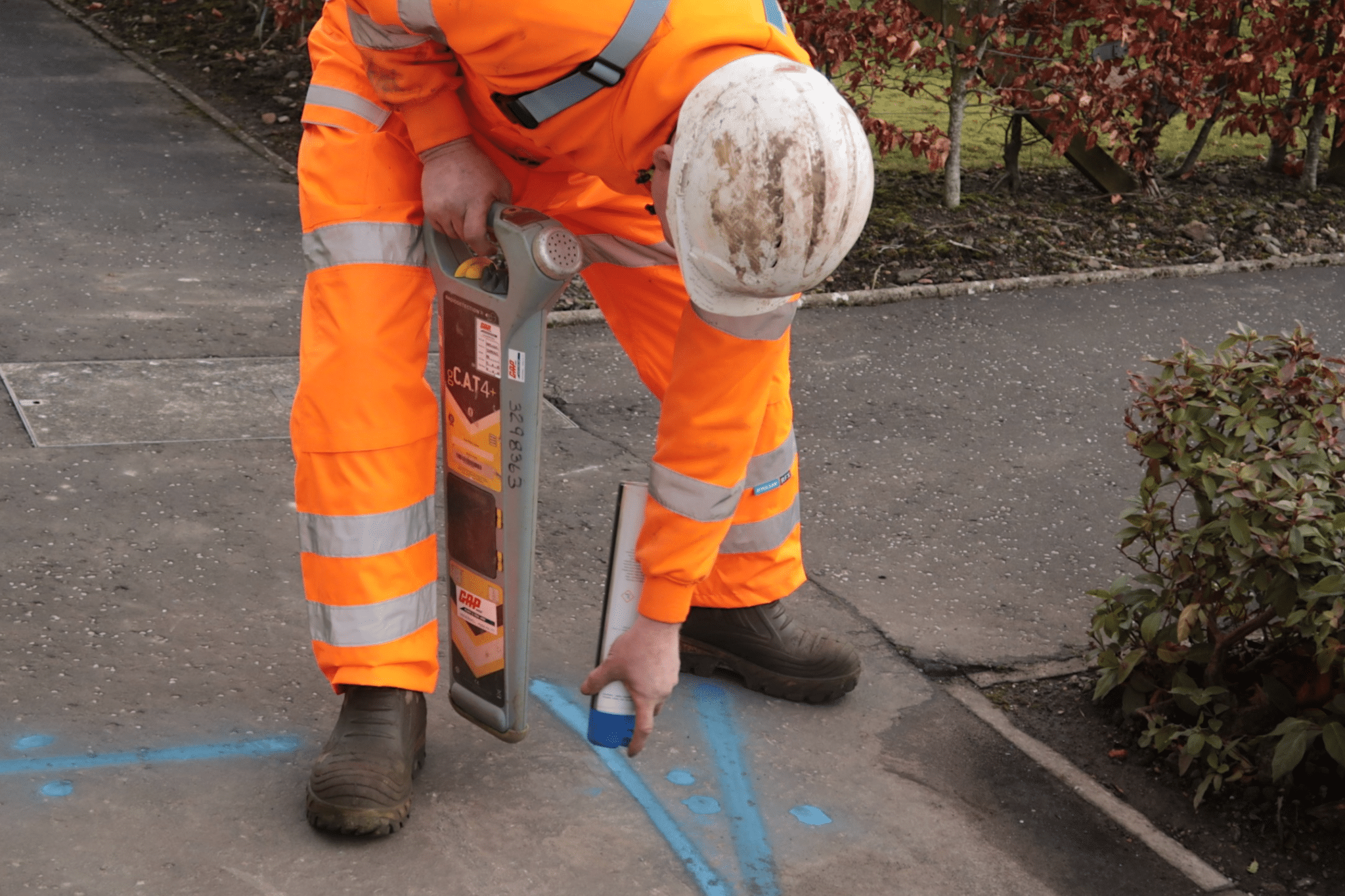 men in a orange high vis spray painting the ground blue