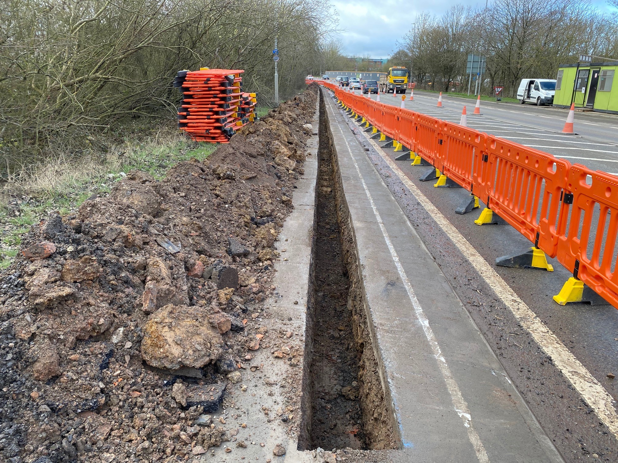 Trench in road that has been dug with safety barriers to the right of it