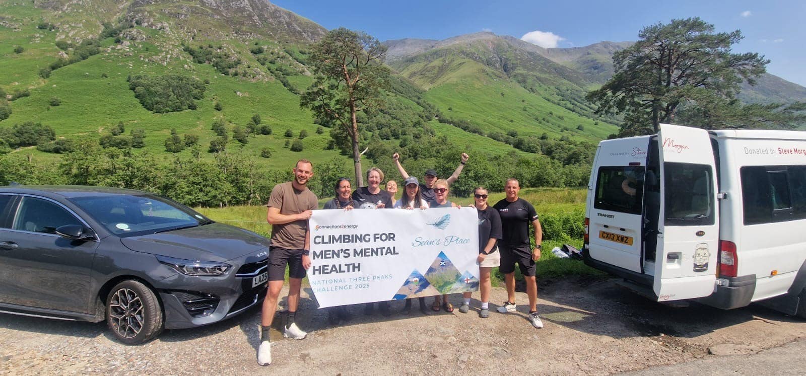 Group of walkers stood in front of Ben Nevis with sign that says 'Climbing for men's mental health'